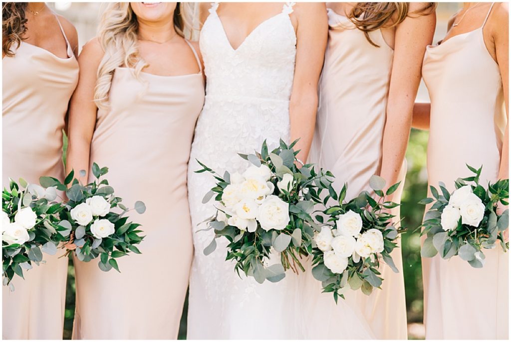 Bride with bridesmaids wearing blush dresses and holding white and green bouquets 