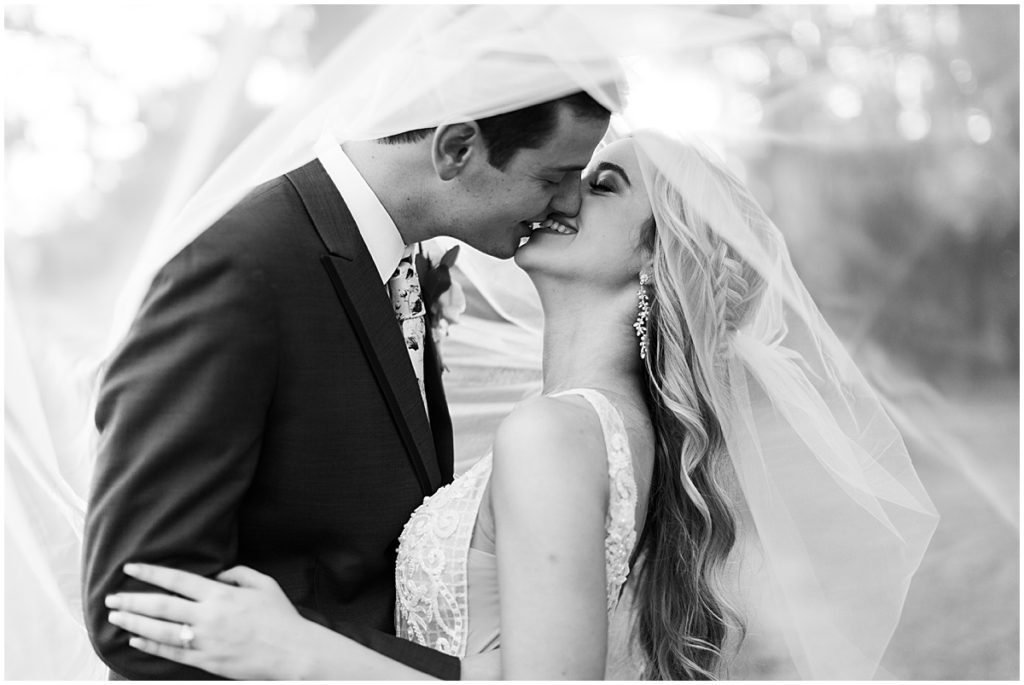 Black and white shot of bride and groom underneath veil