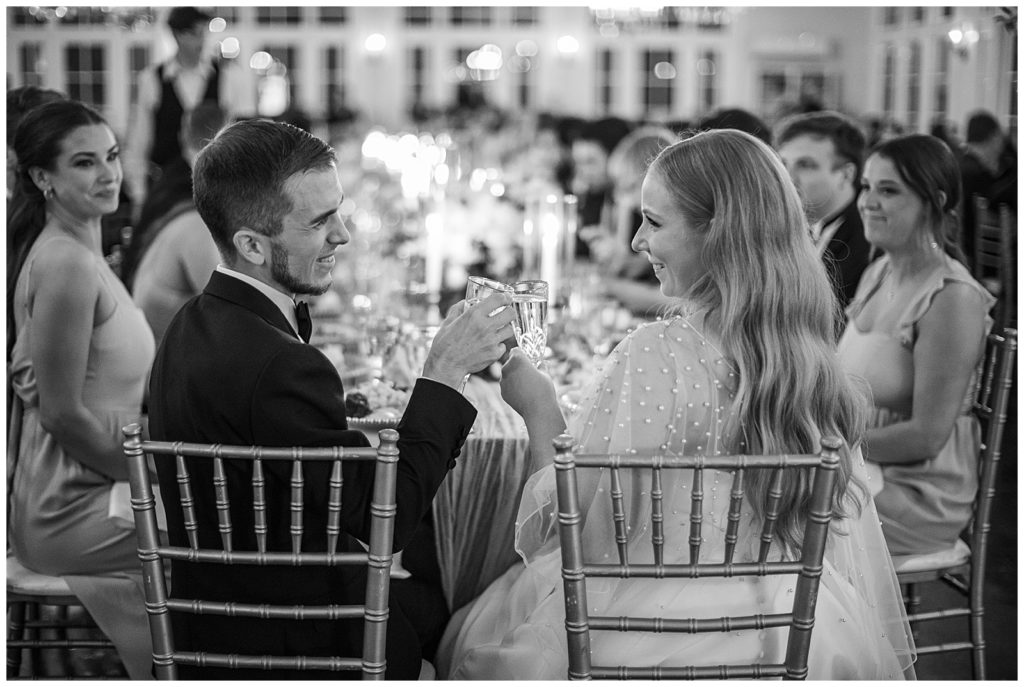black and white photo of bride and groom toasting champagne glasses at their wedding