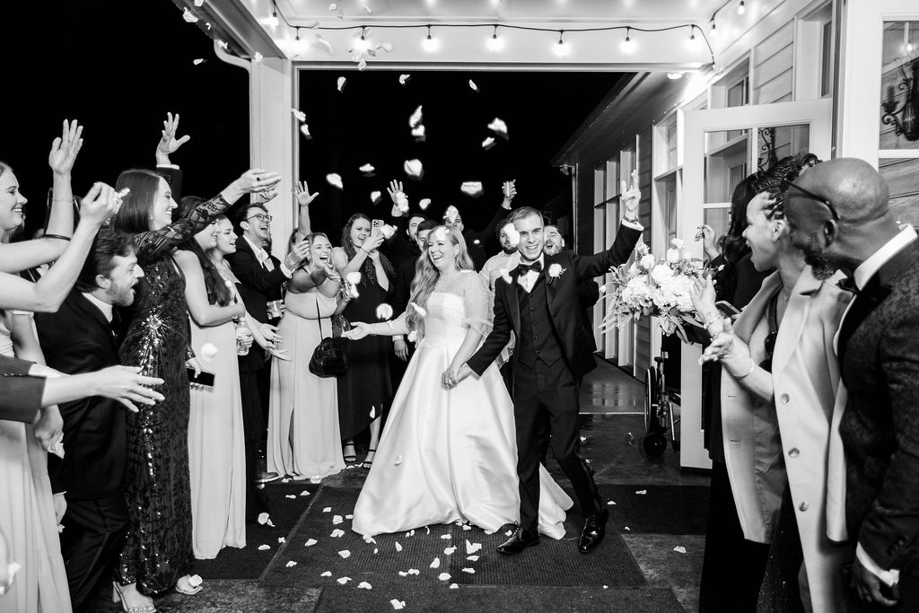black and white photo of bride and groom exiting their wedding with petals being thrown
