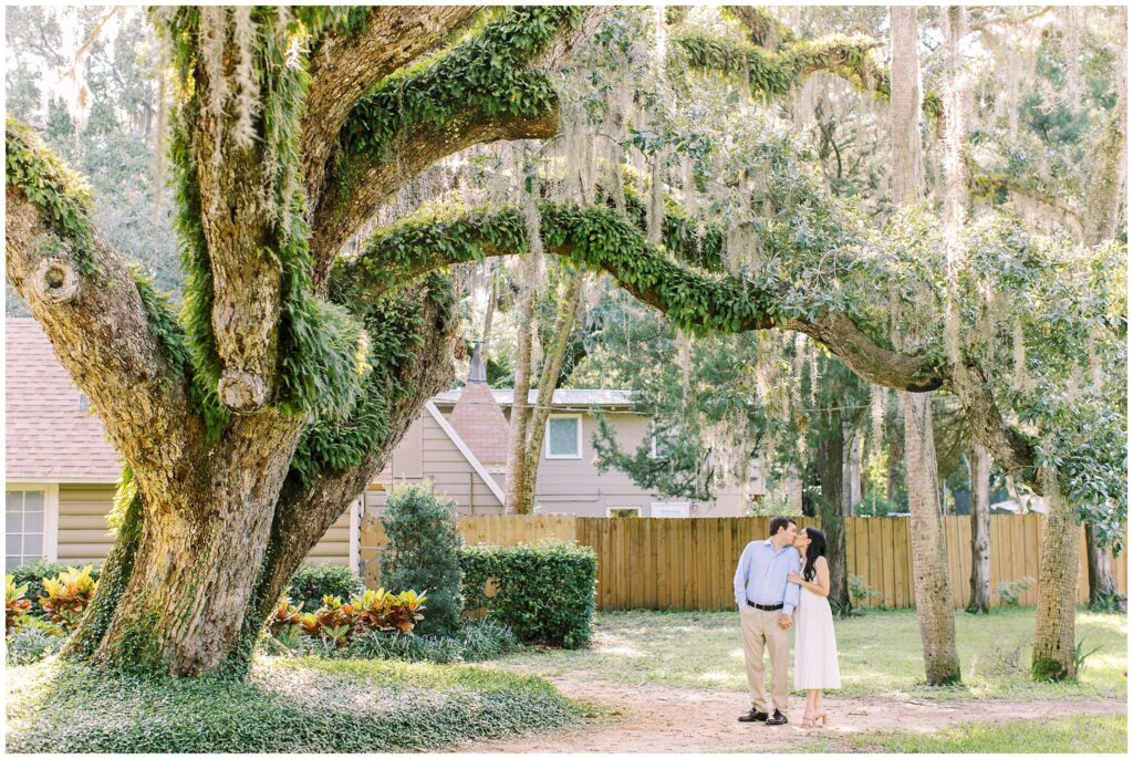 Wide angle couple portrait kissing under a large Oak tree with moss growing on it. 