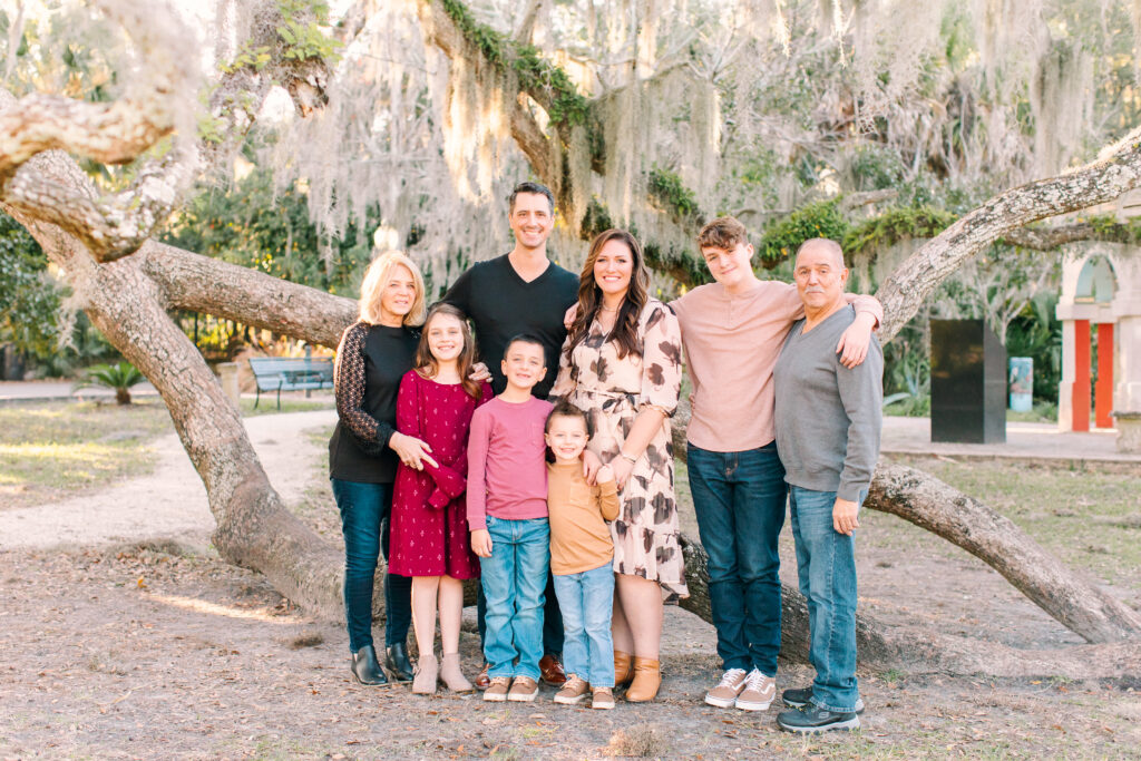 family of six and grandparents standing in front of a large tree smiling at the camera