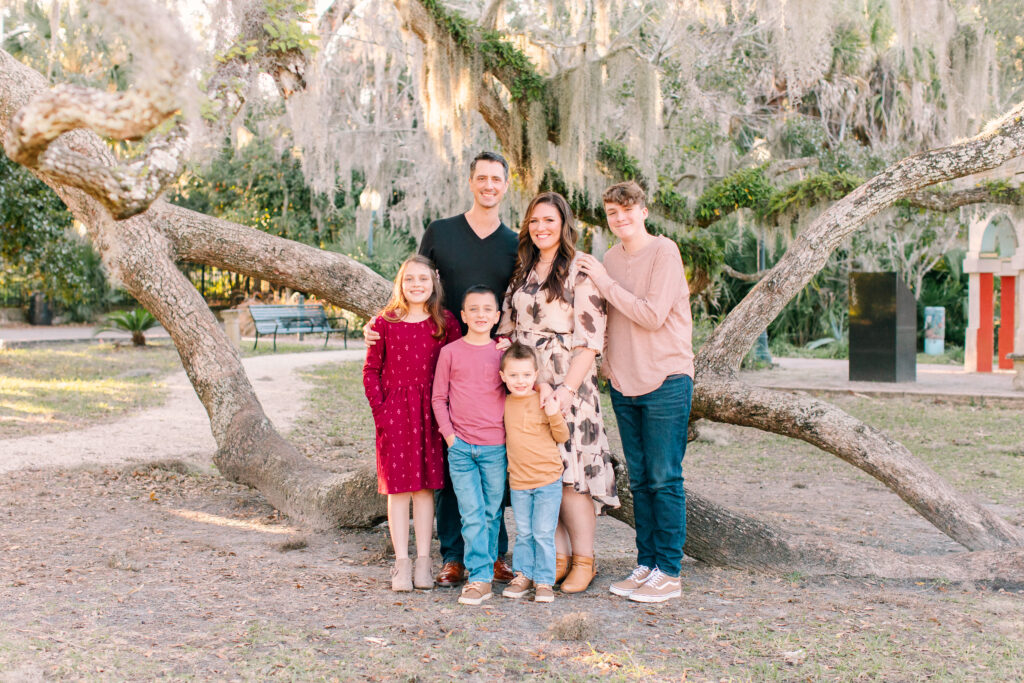 Fall family photo in front of a large tree with the family looking at the camera