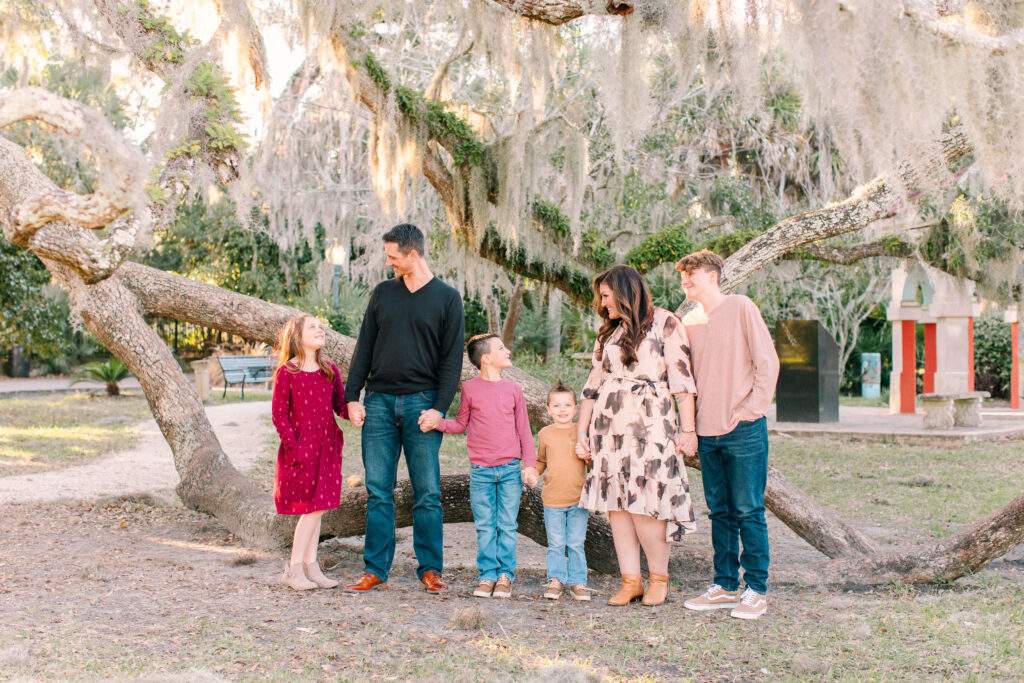 Fall family photo in front of a large tree with the family looking at each other