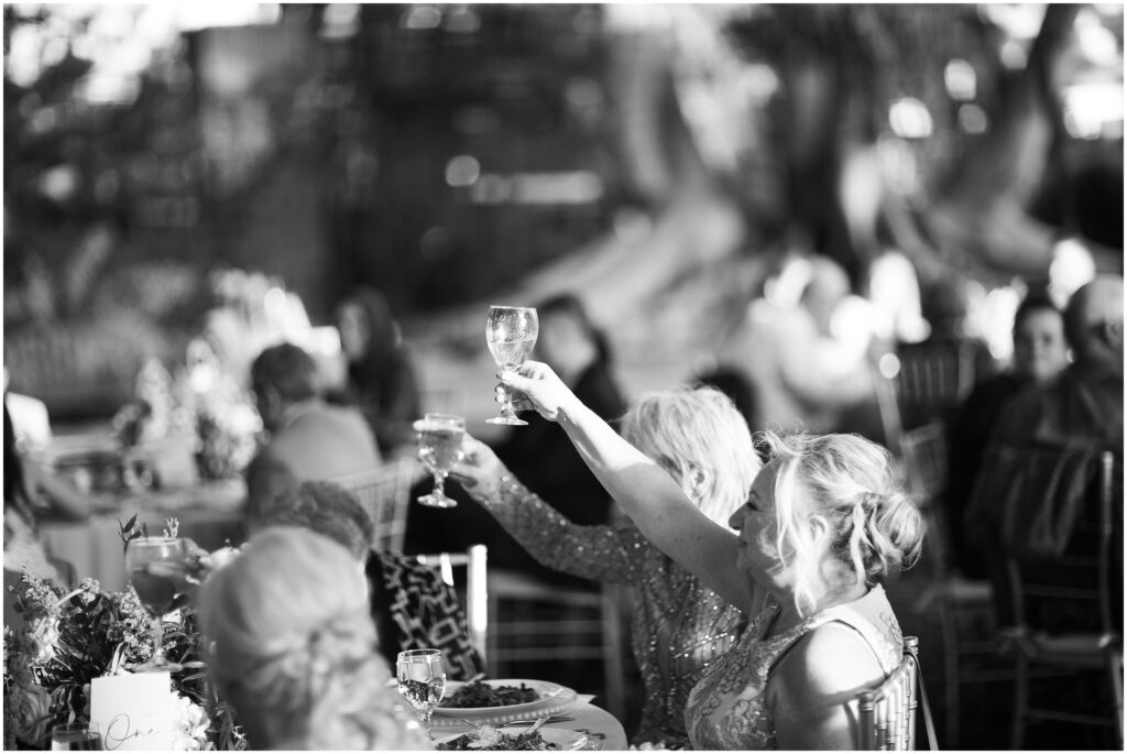 black and white photo of wedding reception guests raising their glasses for a toast 