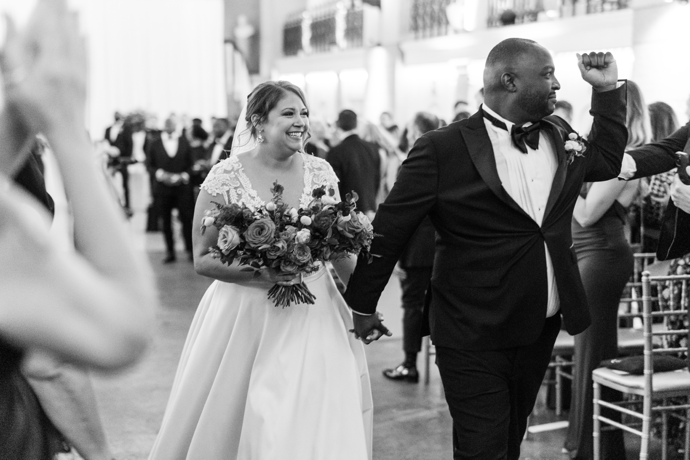 bride and groom recessing down aisle after wedding ceremony while groom pumps fist in the air 