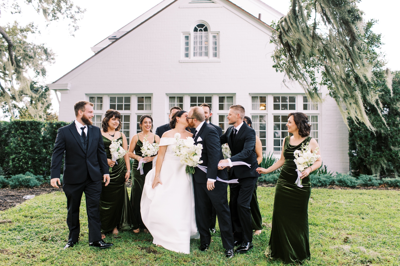 Bride and groom kissing while surrounded by wedding party members