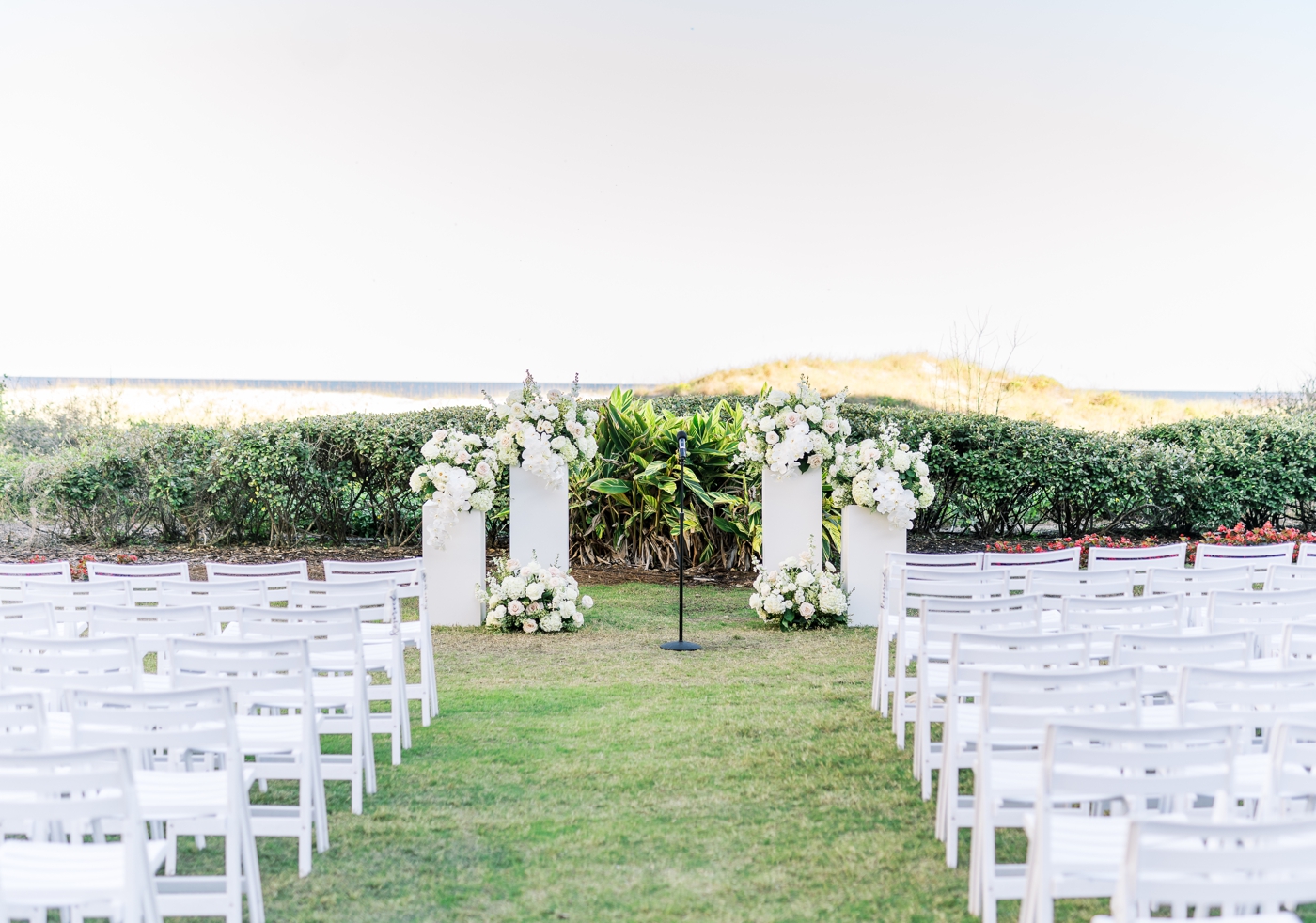 Outdoor reception space at Ritz Carlton Amelia Island with white chairs and four white pillars holding white and green floral arrangements 